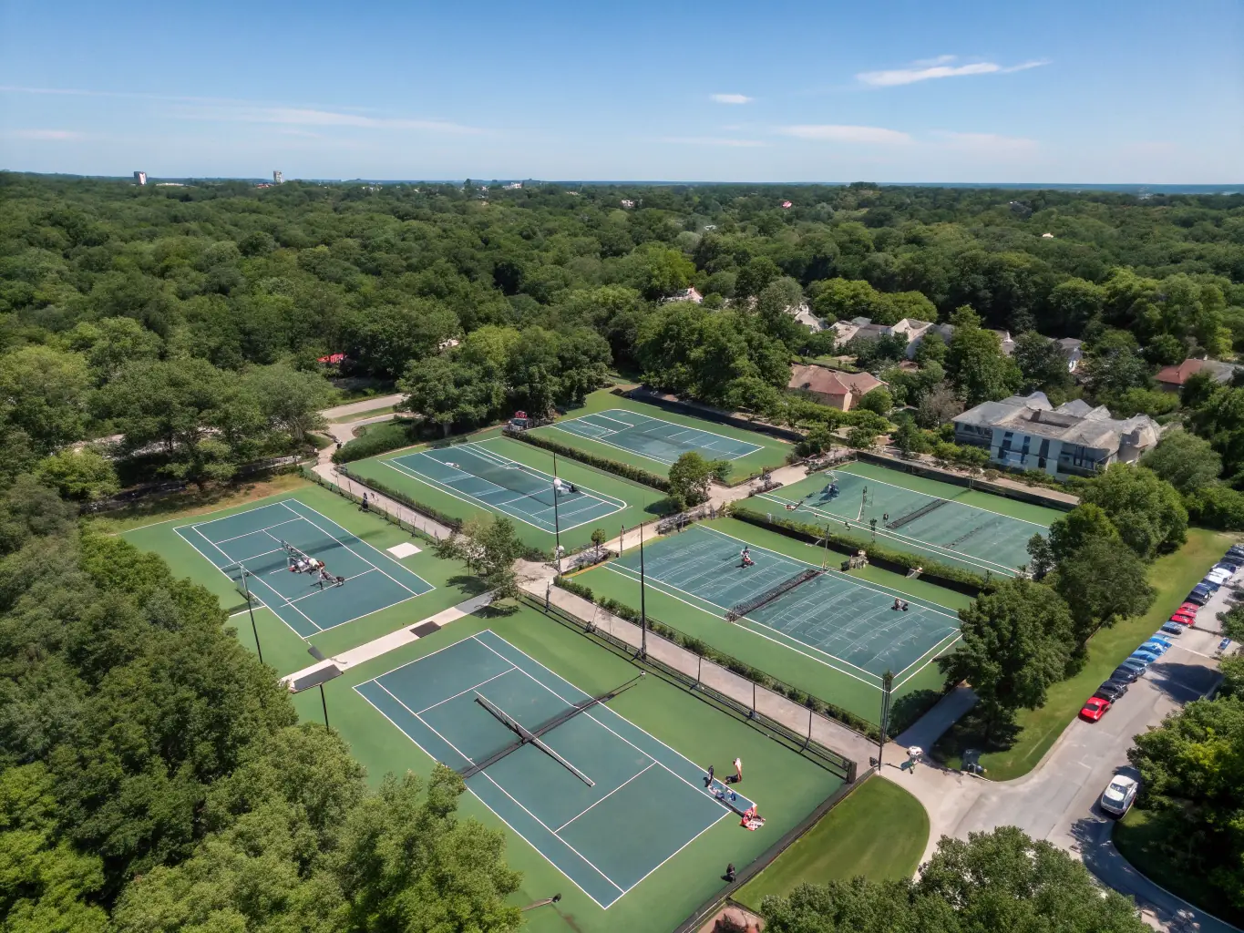 A wide-angle view of the club's modern tennis facilities, showcasing multiple courts in excellent condition, with players engaged in friendly matches and practice sessions.